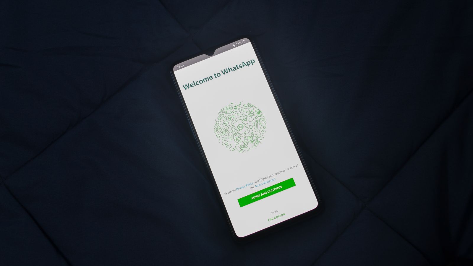 A smartphone lying on a dark bedsheet showing the WhatsApp welcome and registration screen