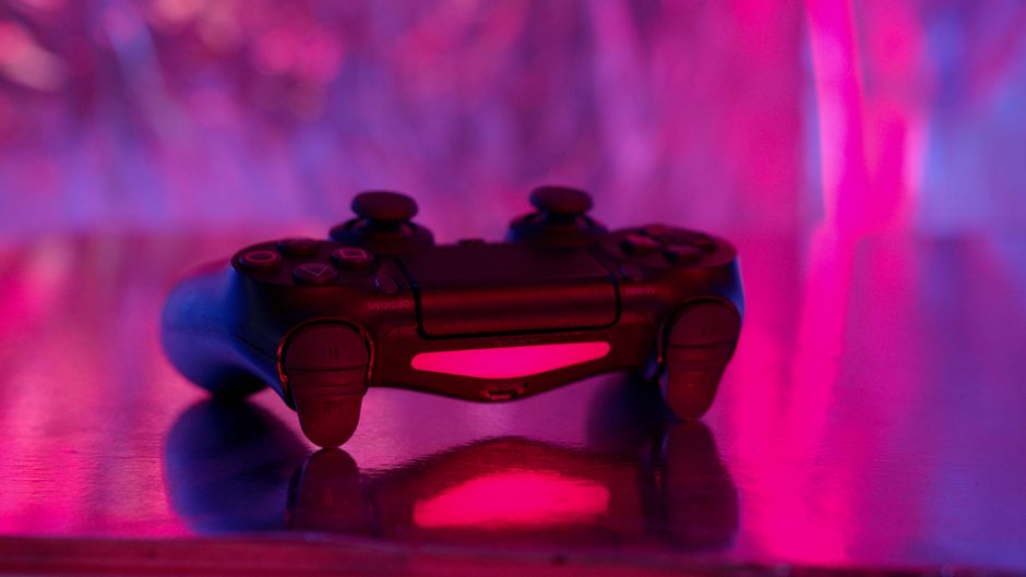 A game controller glowing red and pink on a reflective surface